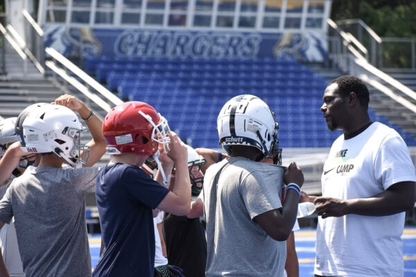 Football coach talking to young players in helmets at Chargers football camp.