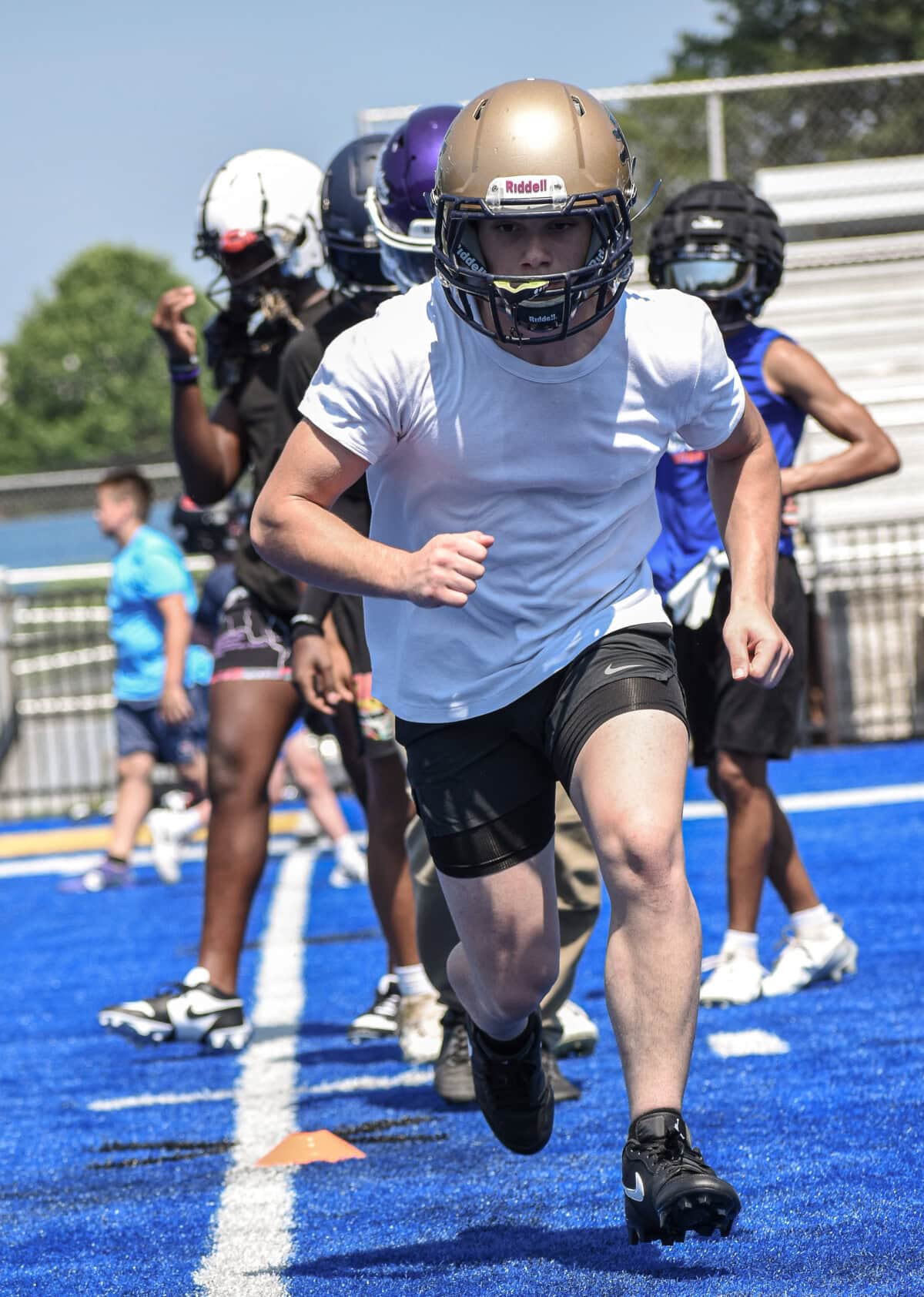 Football player in gold helmet sprints on blue turf during practice.